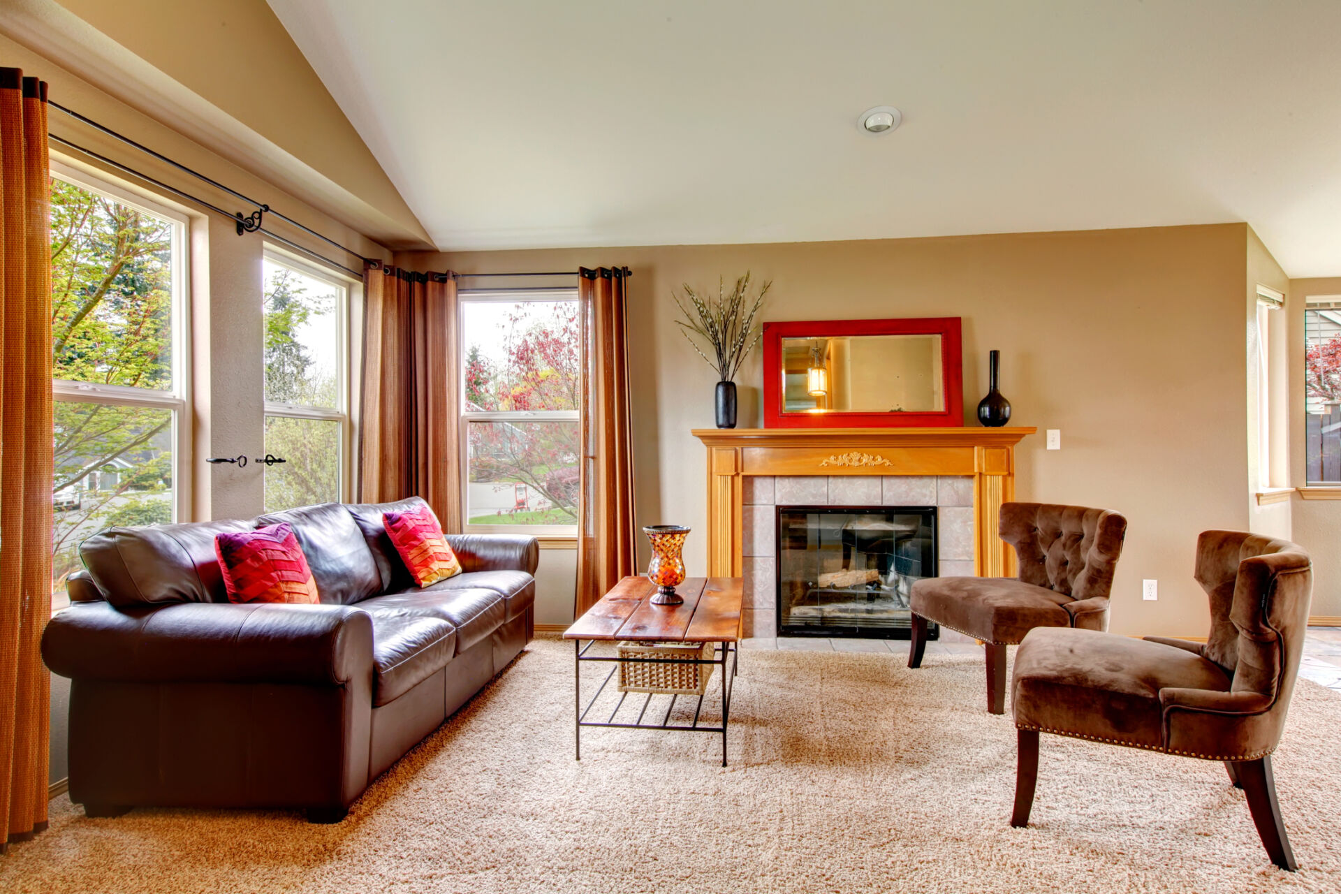 Vaulted ceiling living room with soft carpet floor and cozy fireplace. Furnished with leather couch, antique style chairs and rustic wooden coffee table