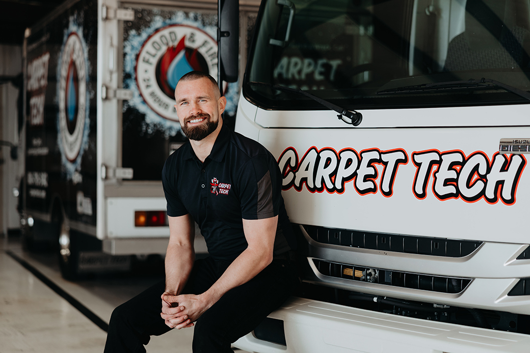 Smiling technician sitting on the bumper of a Carpet Tech van