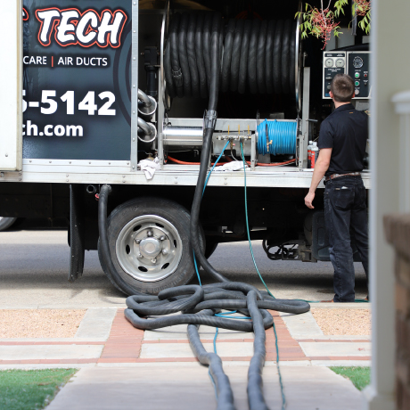 Technician standing with his back to the camera besides a large hose reel in a Carpet Tech cleaning rig.